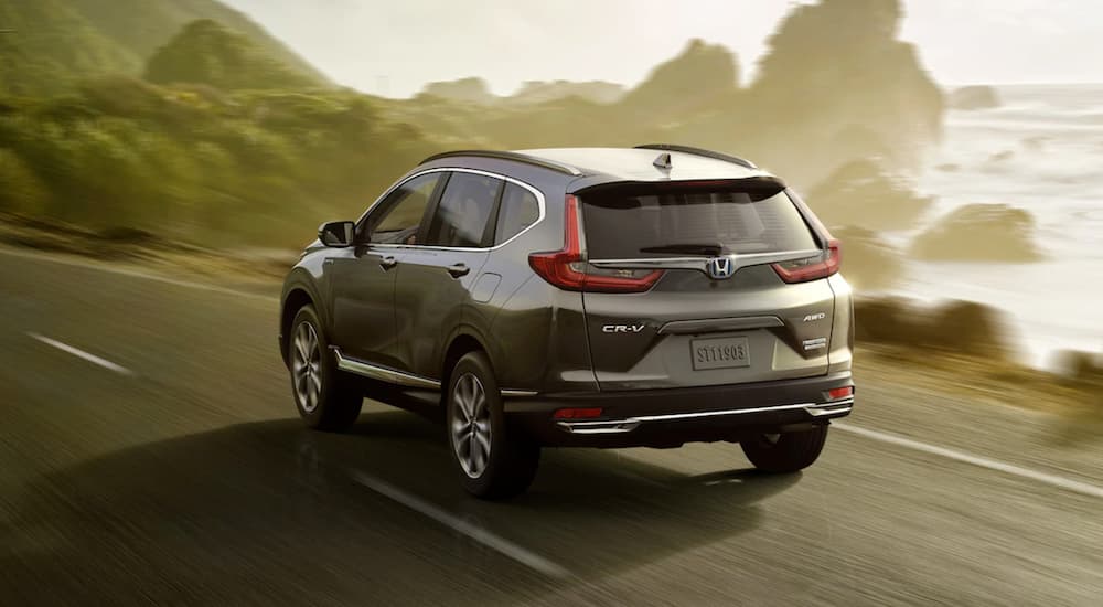 A grey 2021 Honda CR-V is shown from the rear driving past an ocean inlet at sunset.