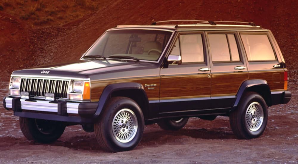 A wood-paneled 1991 Jeep Cherokee is parked in front of red dirt at sunset.