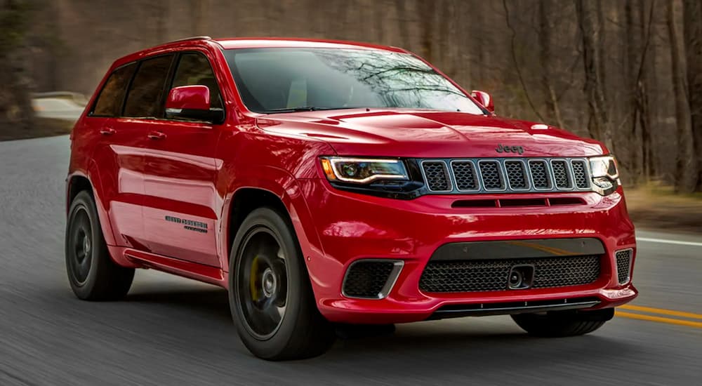 A red 2021 Jeep Grand Cherokee Trackhawk is driving on a winding road in the woods.