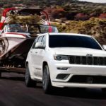 A white 2021 Jeep Grand Cherokee is towing a boat on a rural road.