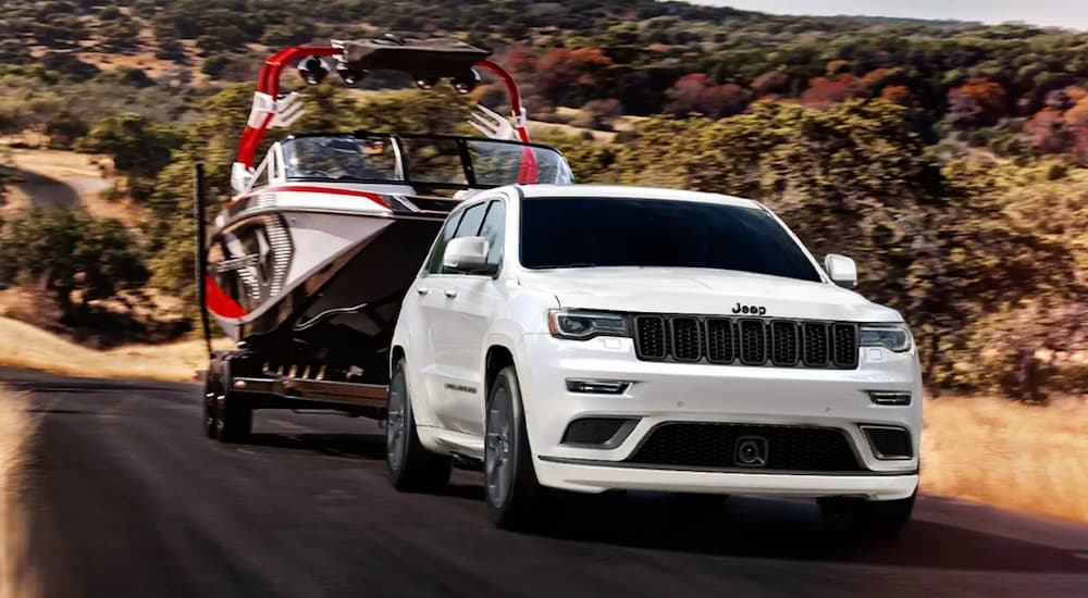 A white 2021 Jeep Grand Cherokee is towing a boat on a rural road.