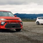 A red and a white 2021 Kia Soul are parked in a lot in front of mountains.