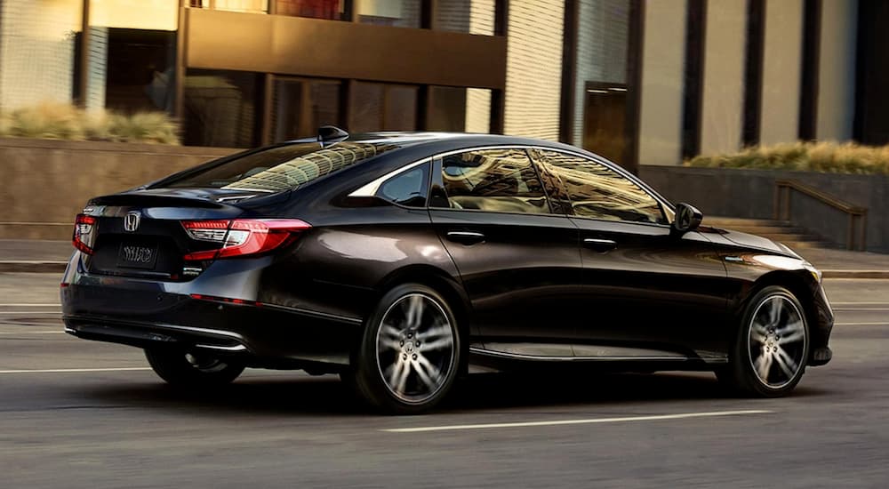 A black 2021 Honda Accord is driving on a city street, shown from the side.