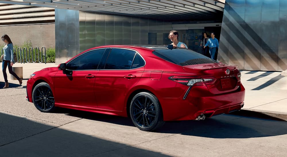 A woman is next to a red 2021 Toyota Camry in front of a city building after it won the 2021 Toyota Camry vs 2021 Honda Accord comparison.