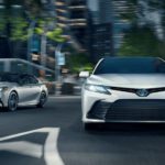 A silver and a white 2021 Toyota Camry are driving on a city street at night.