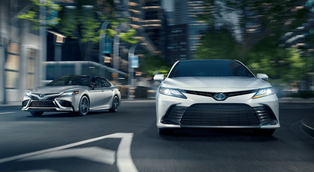 A silver and a white 2021 Toyota Camry are driving on a city street at night.