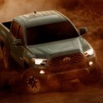 A green 2021 Toyota Tacoma is off-roading in a cloud of dirt after winning the 2021 Toyota Tacoma vs 2021 Jeep Gladiator comparison.