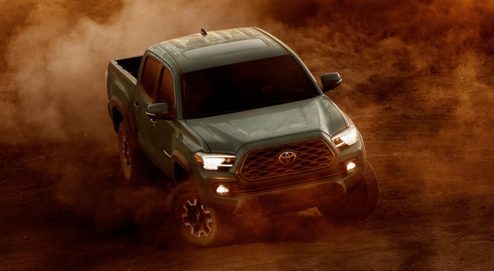 A green 2021 Toyota Tacoma is off-roading in a cloud of dirt after winning the 2021 Toyota Tacoma vs 2021 Jeep Gladiator comparison.