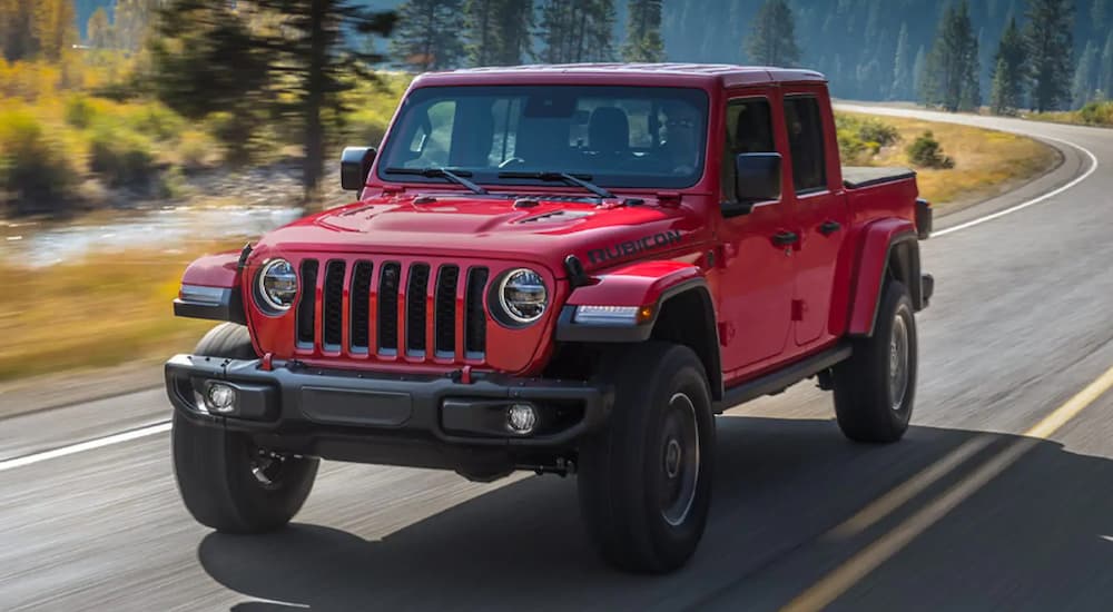 A red 2021 Jeep Gladiator is driving on a road past a corner and trees.