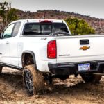 A white 2018 Chevy Colorado ZR2 is shown from the rear off-roading in a muddy field.