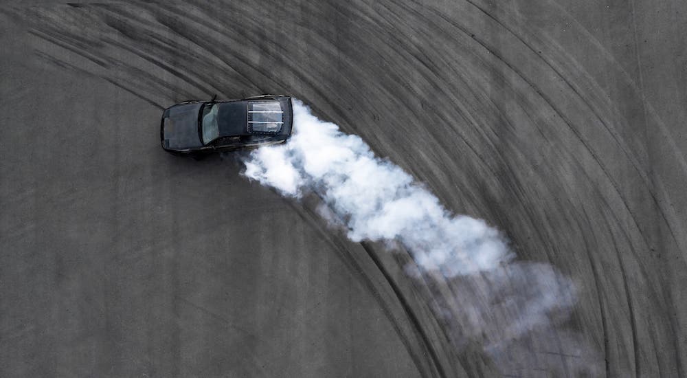 Smoke is coming from the tires on a black car and shown from above.