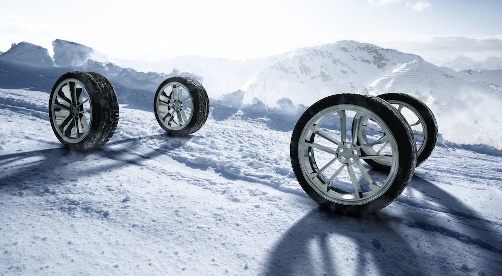 Four tires and rims are on a snowy hill.