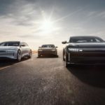 A silver, a gold, and a black Lucid Air are shown from the front driving on a highway.