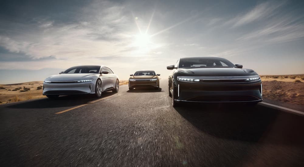 A silver, a gold, and a black Lucid Air are shown from the front driving on a highway.
