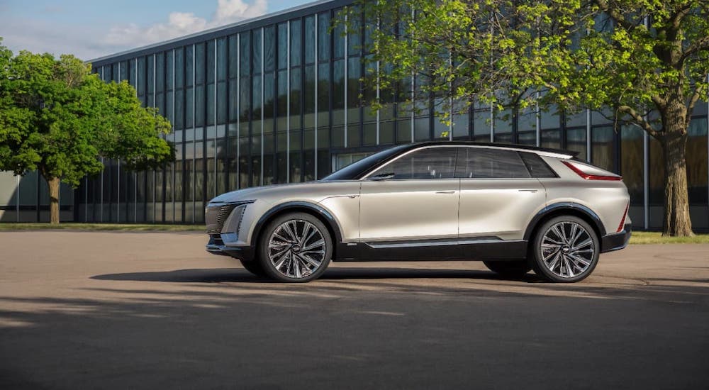 A silver Cadillac Lyriq is shown from the side in front of a glass building.