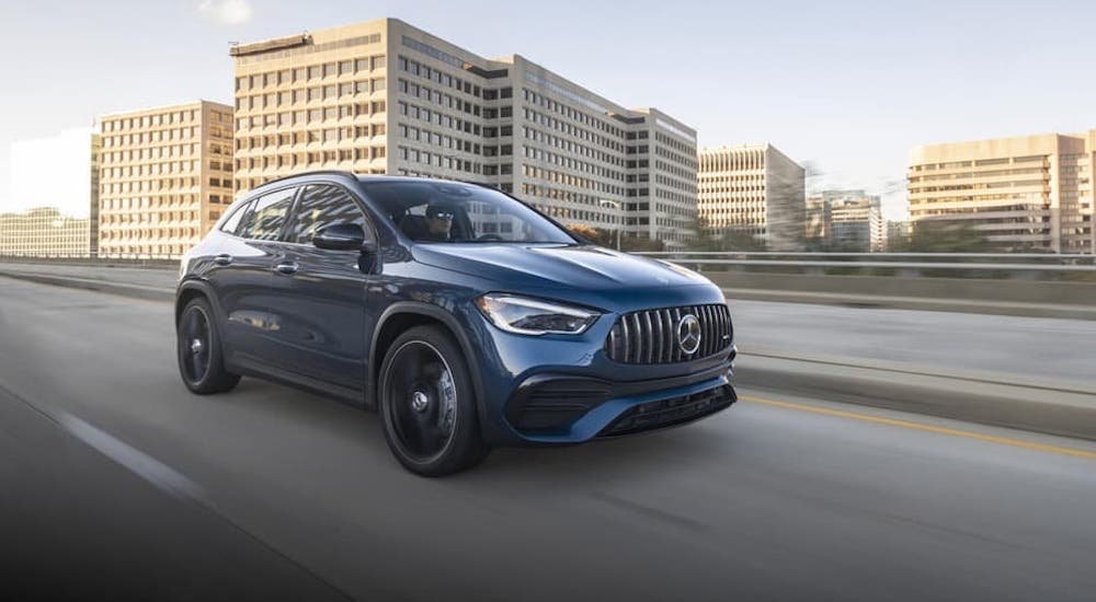 A blue 2021 Mercedes-Benz GLA SUV 250 is driving on a highway in front of a city.