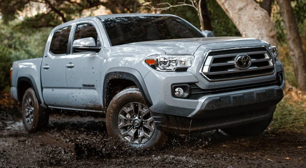 A light grey 2021 Toyota Tacoma is off-roading in the mud in the woods.
