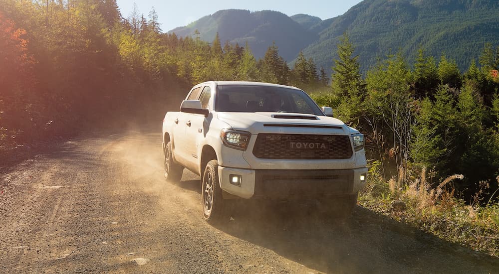 A white 2021 Toyota Tundra TRD is driving on a dirt road with distant mountains.