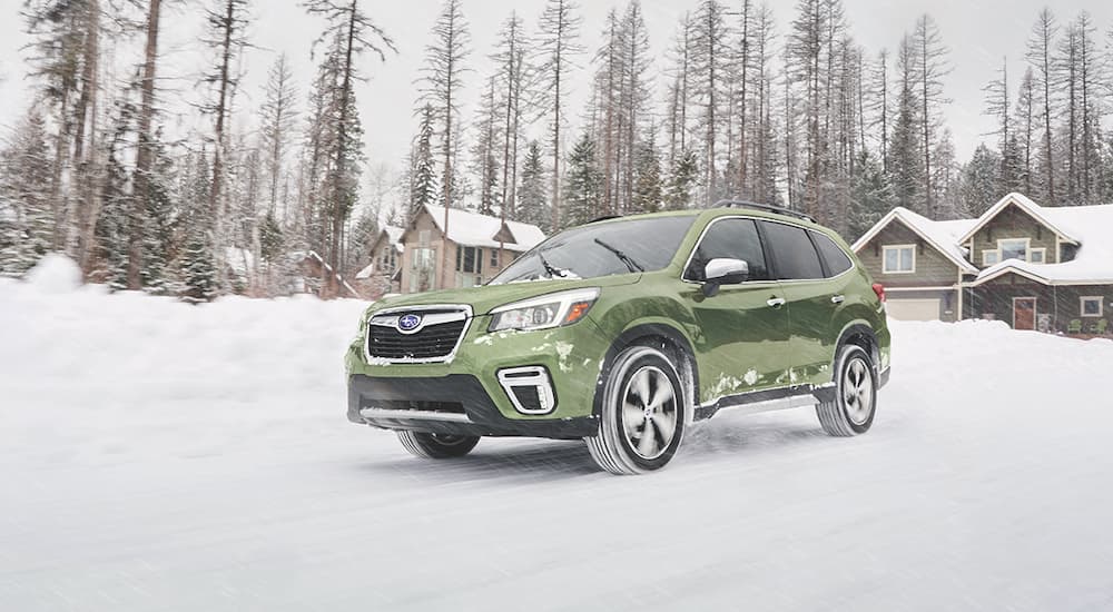 A green 2019 Subaru Forester is driving away from a house on a snow covered driveway.