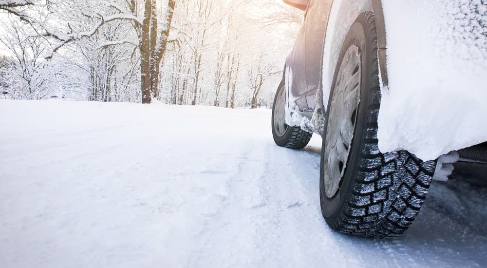 A used car covered in snow and salt is shown at a low angle on a snow covered road.