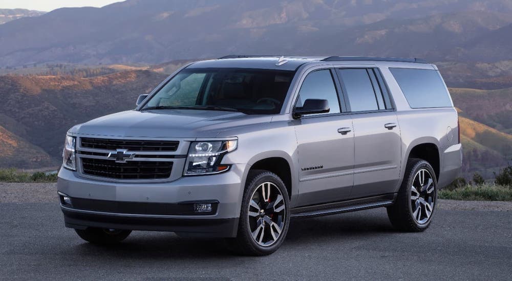 A silver 2019 Chevy Suburban RST is parked in front of mountains.