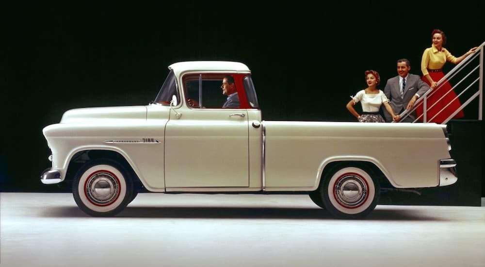 A tan 1955 Chevy Cameo is in a black showroom.
