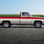 A two-tone orange and white 1973 Chevy Silverado C/K is shown from the side in a parking lot.