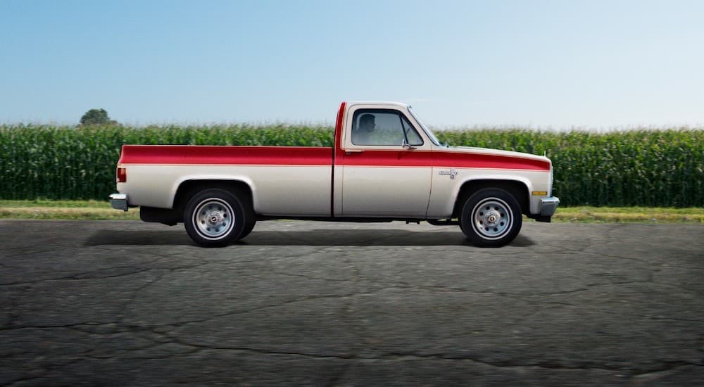 A two-tone orange and white 1973 Chevy Silverado C/K is shown from the side in a parking lot.