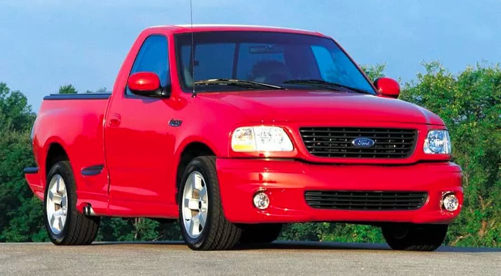 A classic used Ford truck for sale, a red 2002 Ford F-150, is parked in front of trees.