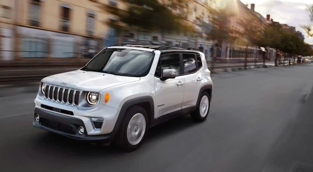 A common sight at a used Jeep dealer near you, a white 2019 Jeep Renegade, is shown driving on a city street.