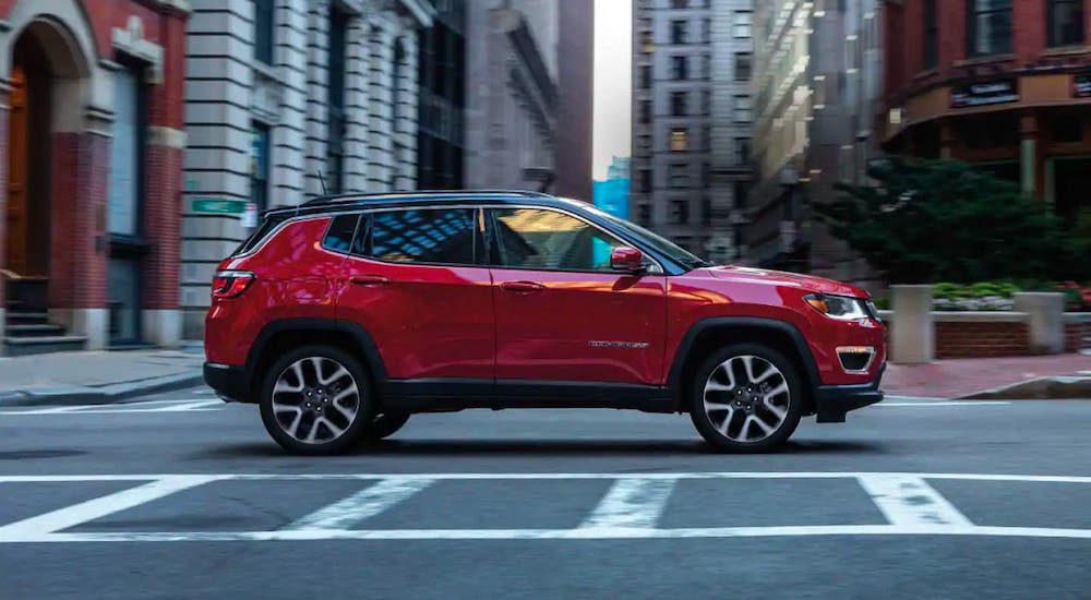 A red 2020 Jeep Compass is shown from the side driving in a city.