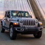 A silver 2020 Jeep Wrangler Unlimited is driving on a bridge at dusk.