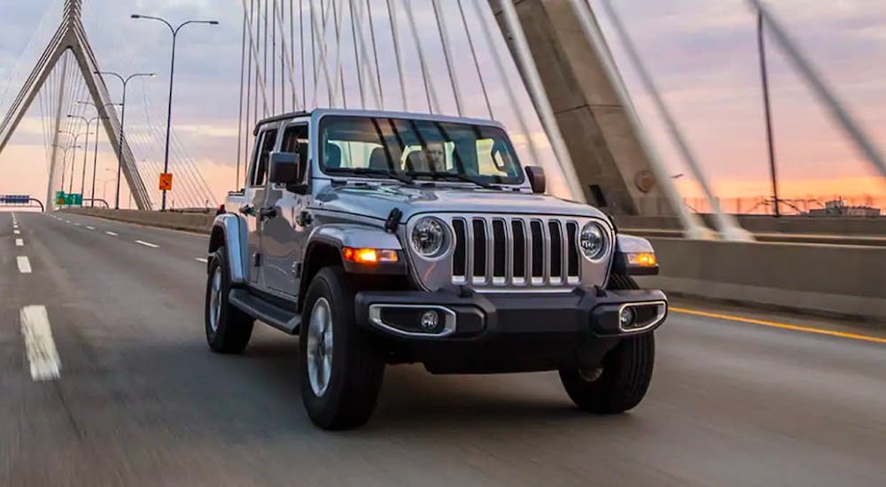 A silver 2020 Jeep Wrangler Unlimited is driving on a bridge at dusk.