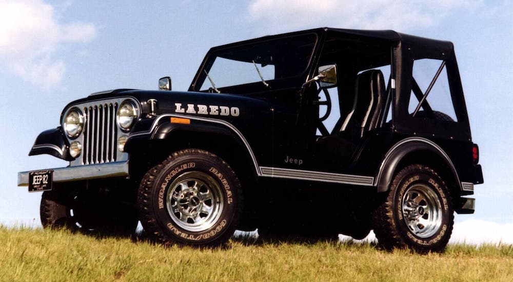 A black 1980 Jeep CJ-7 Laredo is parked on a hill against a cloudy blue sky.