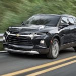 A black 2021 Chevy Blazer is driving past a guard rail and trees.