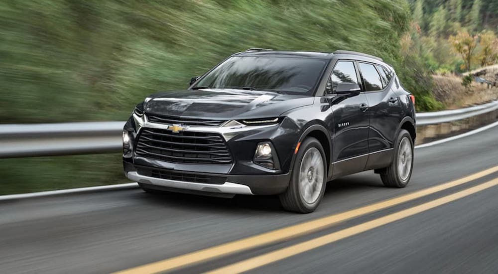 A black 2021 Chevy Blazer is driving past a guard rail and trees.