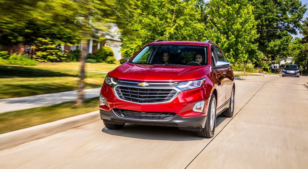 A red 2021 Chevy Equinox is driving on a suburban street.