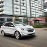 A white 2021 Chevy Equinox is driving in a city.