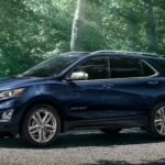 A blue 2021 Chevy Equinox is parked in a driveway in front of trees after winning the 2021 Chevy Equinox vs 2021 Jeep Compass comparison.