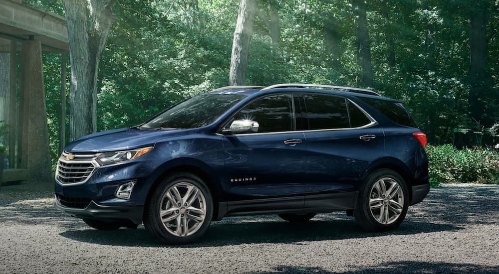 A blue 2021 Chevy Equinox is parked in a driveway in front of trees after winning the 2021 Chevy Equinox vs 2021 Jeep Compass comparison.