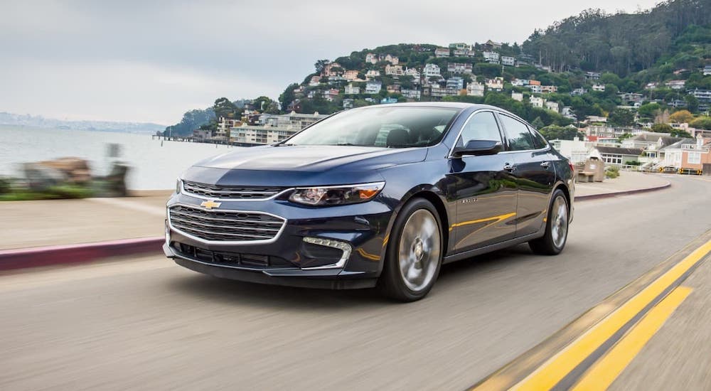 A blue 2021 Chevy Malibu is driving next to a body of water.