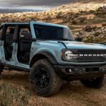 A blue 2021 Ford Bronco 4 door is off-roading in the desert with no doors.