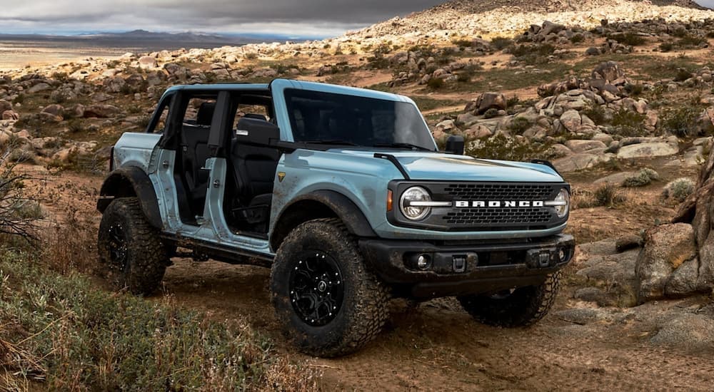 A blue 2021 Ford Bronco 4 door is off-roading in the desert with no doors.