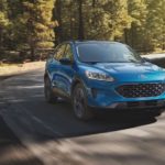 A blue 2021 Ford Escape is driving on a winding road in the woods.