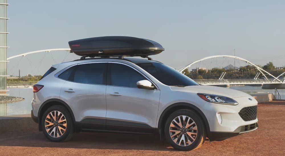 A white 2021 Ford Escape is shown from the side with a luggage container on the roof.
