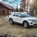 A silver 2021 Ford Explorer is parked in front of a log cabin and a group of mountain bikers.