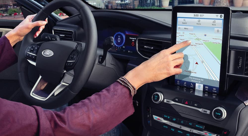 A closeup shows a driver of a 2021 Ford Explorer using the navigation on a large infotainment screen.