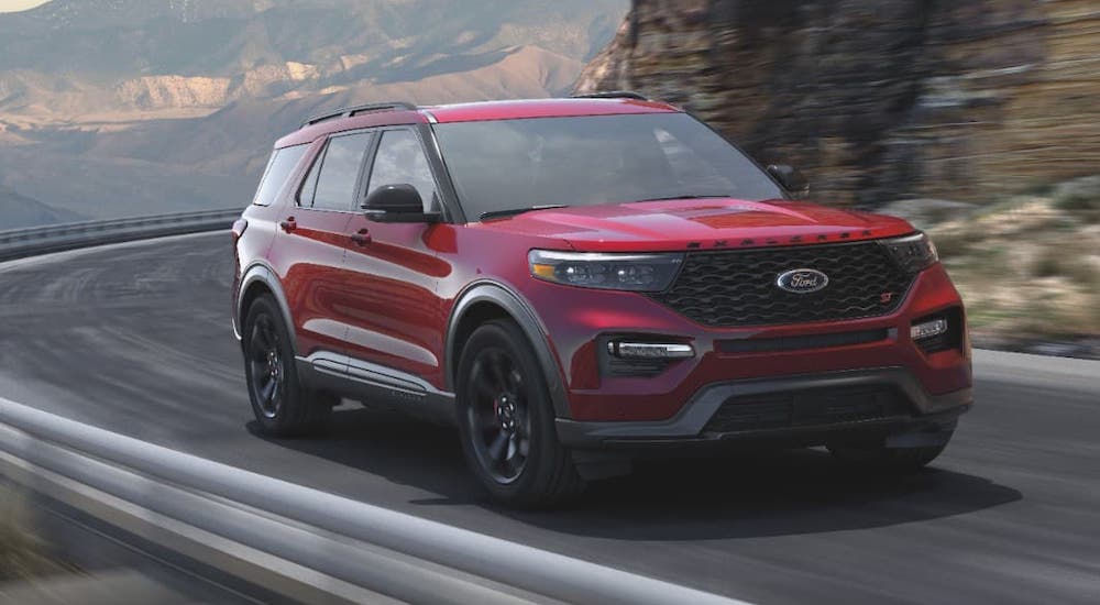 A red 2021 Ford Explorer ST is driving on winding highway next to a rock face.