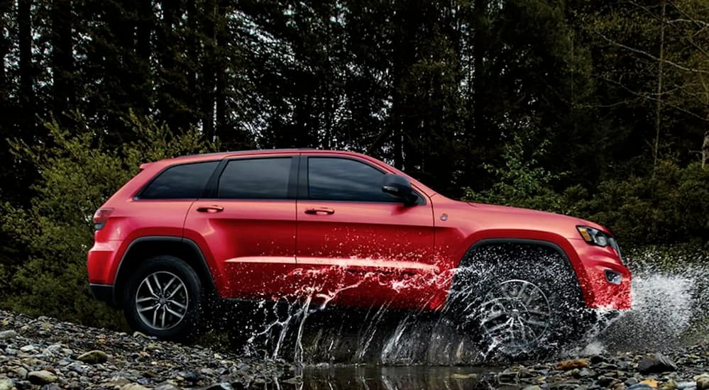 A red 2021 Jeep Grand Cherokee is crossing a river while off-roading.