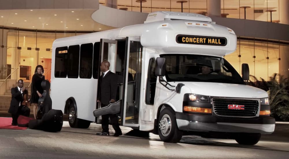 One of the popular 2021 GMC commercial vehicles, a white 2021 GMC Savana Cutaway is shown as a bus to a concert hall.